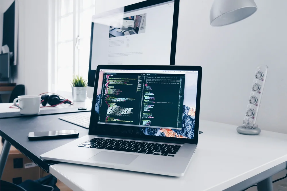 A laptop displaying source code in a naturally lit software workspace